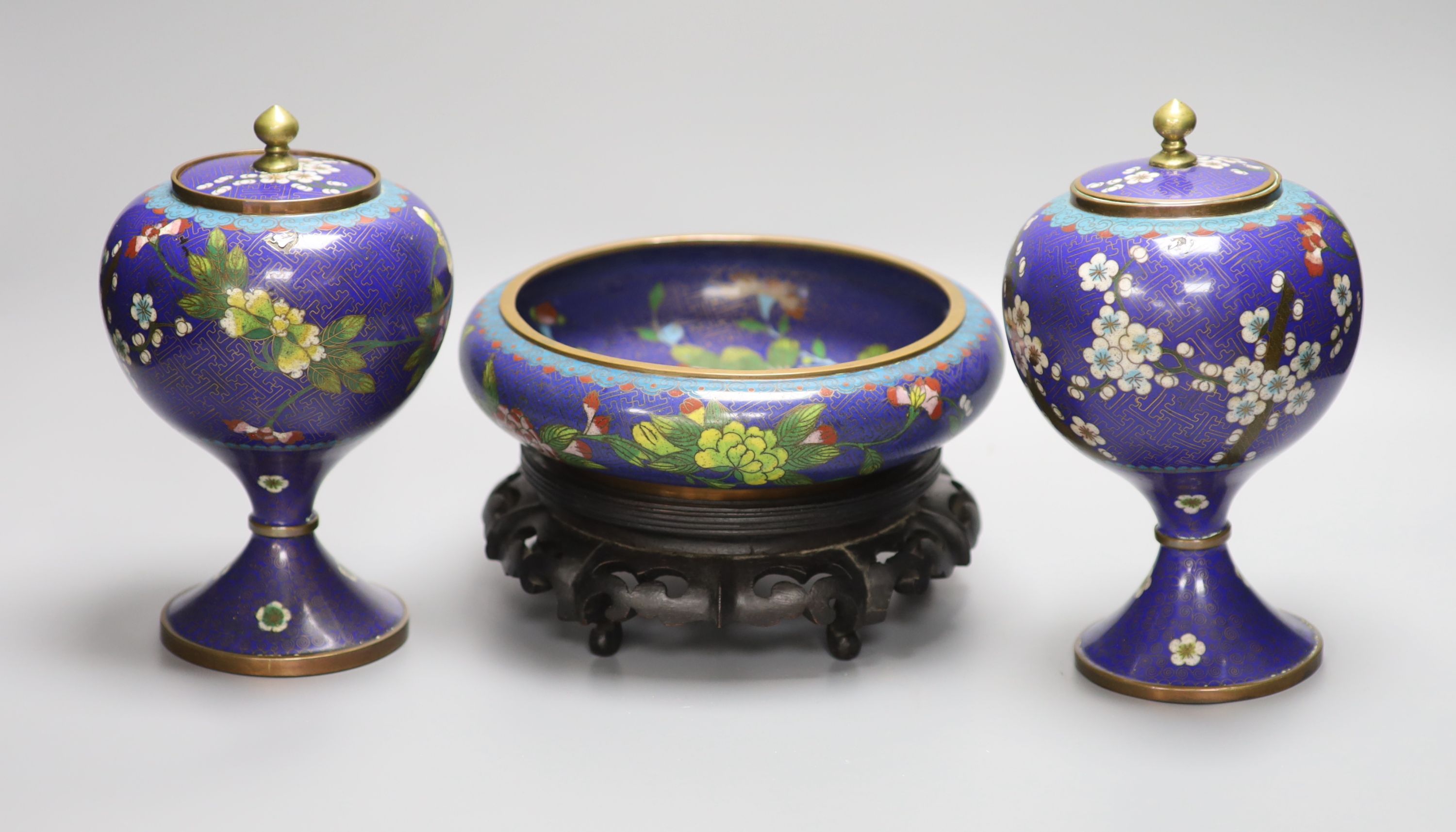 A pair of early 20th century Chinese cloisonne enamel jars and covers and a similar bowl and wood stand, tallest 20cm